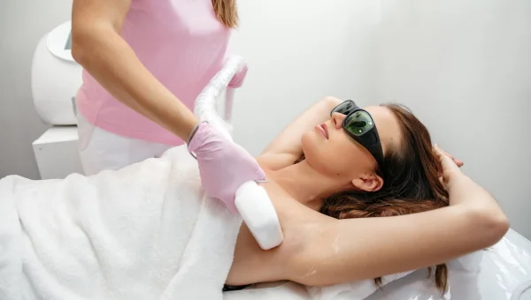 Woman receiving laser hair removal on her armpit while wearing protective glasses.