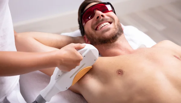 Man receiving laser hair removal on his armpit while smiling and wearing protective glasses