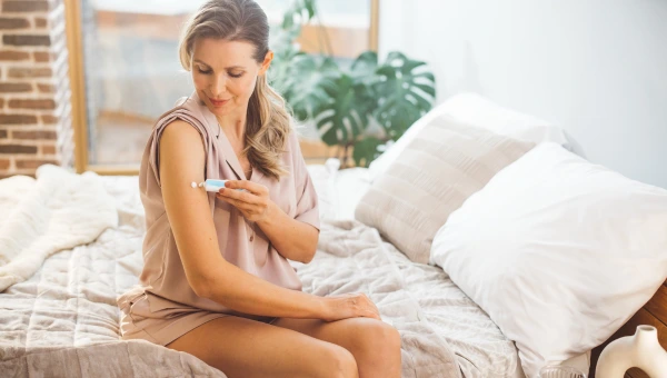 Woman applying hormone therapy cream on her arm in a cozy bedroom