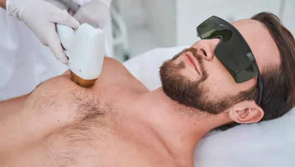 Man receiving laser hair removal on chest, wearing protective eyewear.