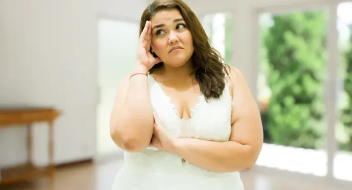 Worried plus-size woman in a white dress standing indoors